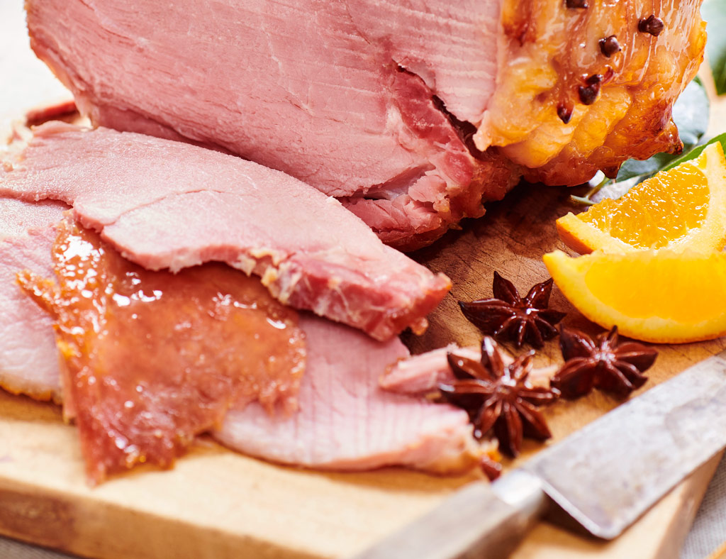 Sliced Champagne-Glazed Maple Ham with anise pods and orange aside.