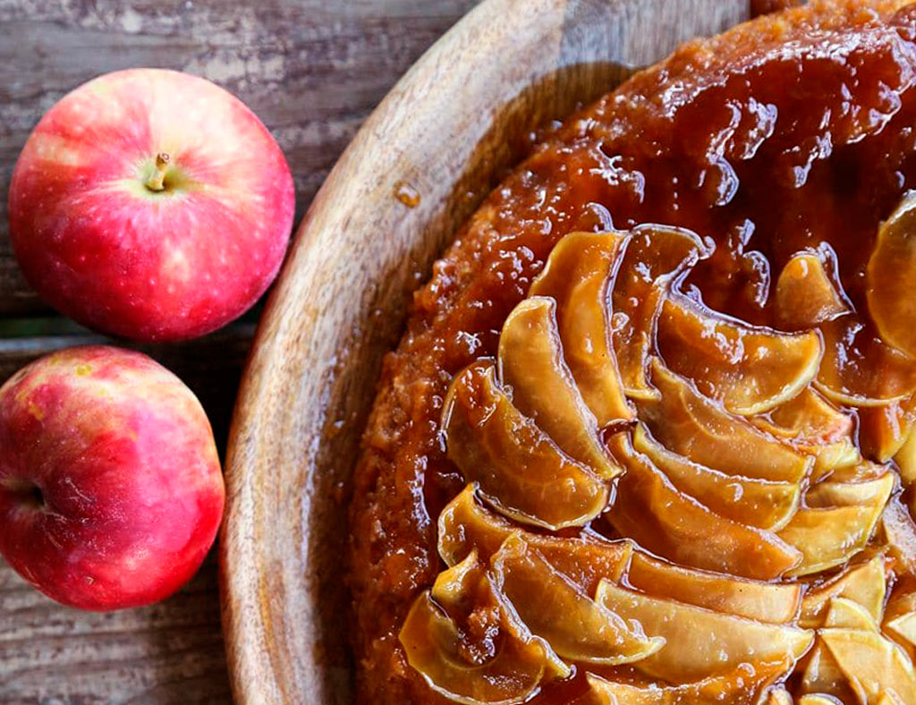 Maple Upside-Down Cake with two red apples on the table on the left